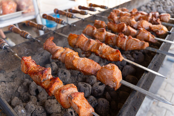 A large outdoor grill with many skewers of juicy, freshly grilled shashlik meat cooking over hot coals.