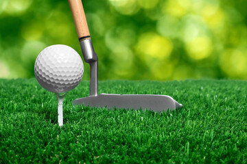 Golf ball, tee, club and green grass against blurred background