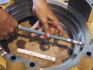 Close-up of a person's hands using a Tubular inside micrometer to measure a drum piston. The image focuses on the industrial process, highlighting precision, quality, and the technical tools involved.