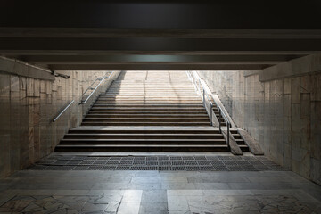 Empty underground pedestrian passage with marble walls and stairs leading to daylight, urban metro tunnel infrastructure detail.
