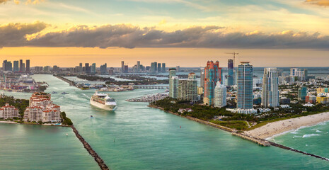 Obraz premium Luxurious cruise ocean liner sailing at Miami port harbor through main channel near South Beach. Hotels and residential buildings on waterfront and high skyscraper towers of downtown in distance