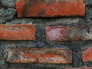 Close-up view of an old red brick wall with rough cement texture.