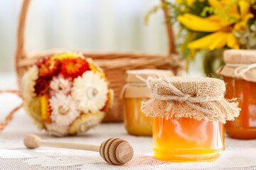Jars of honey and beautiful autumn flowers and plants in the background.