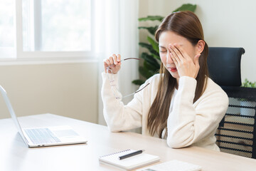 Eye problem concept, fatigue asian young woman tired eyes, irritated rubbing eye dry relief vision pain after work on laptop computer, eye strain, hand holding glasses, suffer migraine, bad blurry.
