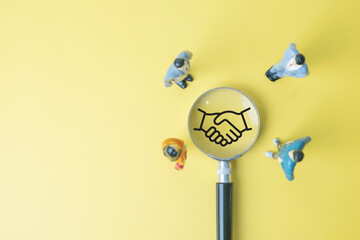A team of miniature figures focuses on a handshake icon. A concept for teamwork, collaboration, and building a business partnership. A symbol of trust, respect, and mutual agreement.,copyspace.
