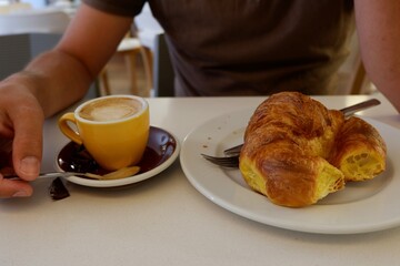 A person sits at a small table in a cafe, savoring a warm croissant and sipping a rich cup of coffee.