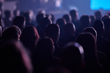 Audience backlit by blue purple lights at Gdynia corporate event, landscape telephoto, shallow depth, moody ambiance, great for webinar and training advertisement