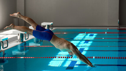 Swimmer entering water with powerful streamlined body position at start. Concept of motivational posters, sports advertising, swimming education, fitness wellness, and rehab training context.