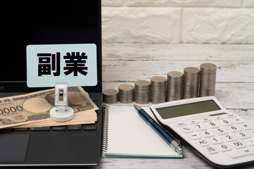 ノートパソコンと積みあがったコインと電卓で副業のイメージ
