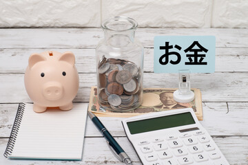 豚の貯金箱と広口瓶の小銭と電卓とノートでお金のイメージ
