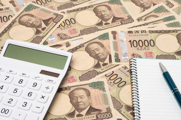 多数の一万円札上に置かれた電卓とノートとペン