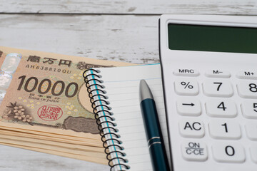 積み重ねた一万円札と電卓とノートで見積もりのイメージ