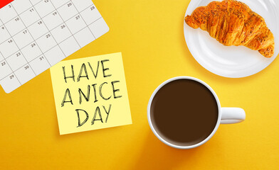 Morning coffee, croissant and card with HAVE A NICE DAY wish on the orange background