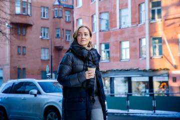 Middle aged woman walking along snowy city street with coffee cup, cozy winter urban lifestyle,...