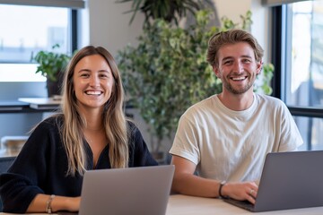 Happy young professionals working on laptops in modern green office. Smiling man and woman sitting at desk, concept of coworking, startup culture and digital collaboration