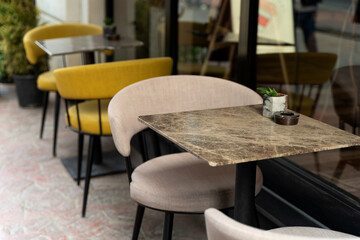 Cozy outdoor cafe scene featuring modern furniture with stylish yellow and beige chairs, a marble table, and potted plants, creating an inviting atmosphere for relaxation and socializing