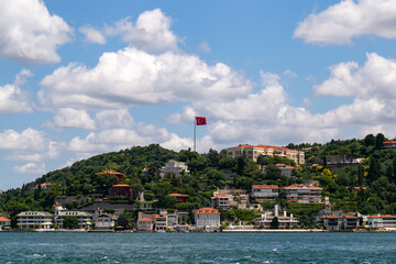 Scenic waterfront view showcasing lush green hillside dotted with elegant homes, under a bright blue sky with fluffy clouds, embodying the essence of travel and discovery in serene environments