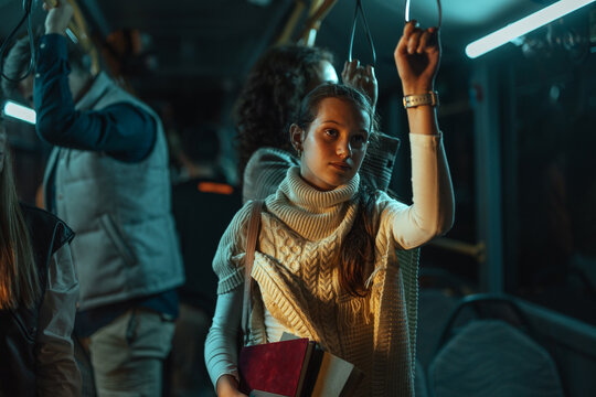 Young woman holding books on a dimly lit bus