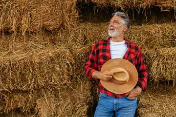 Old farmer standing in front of bales of hay