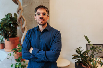 Confident businessman crossing arms in modern office with plants