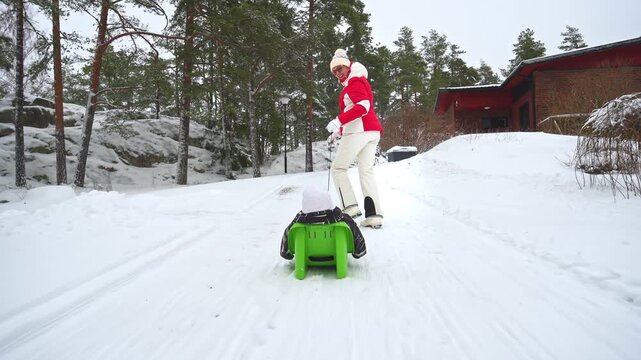Grandmother pulling child on sled in snowy Finland, enjoying winter family lifestyle outdoors. Warm clothing, joy, love, and seasonal holiday atmosphere in bright daylight.