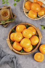 Fresh Sweet Persimmons in Wicker Baskets with Green Leaves on Rustic Table - Autumn Fruit Harvest Display