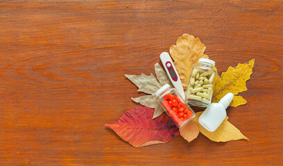 Medicines for prevention and treatment of autumn diseases, viral infections, colds. Vitamins in tablets, food supplements in capsules, nasal spray, thermometer on fallen leaves. Copy space, flat lay