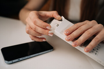 Close-up hands of happy woman with manicured nails carefully opening white retail package containing new phone adapter cable, ready to connect and charge. Concept of smartphone unboxing process.