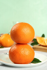 Fresh Orange Citrus Fruits Stacked on White Plate with Green Leaves