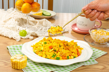 Golden scrambled eggs with fresh corn kernels and vegetables on wooden table breakfast meal