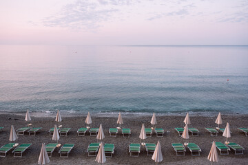 View from above on brown straw umbrellas and green sun loungers. Beautiful sunny summer day in sea resort. Vacations and travel concept