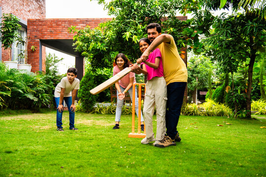 Indian Asian family bonding through outdoor cricket batting in garden, enjoying fun and play