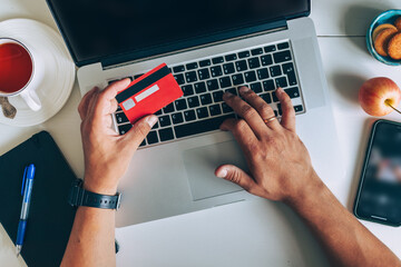Man using laptop and holding credit card on desk with coffee cup and notebook. Concept of online shopping, ecommerce and digital payment.
