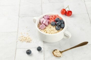 Healthy oatmeal breakfast bowl with fresh fruit, yogurt chunks and berries on white wooden table
