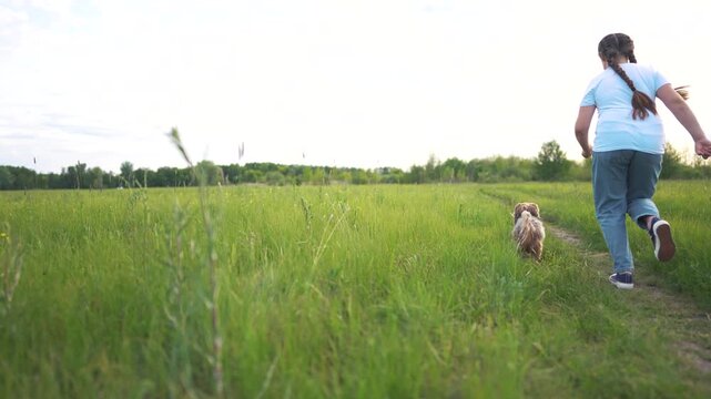 Young girl running with dog. Girl is running outside with a dog. A casual back-view on nature and friendship. A little girl sprinting alongside a dog lifestyle.