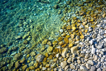 Turquoise rippling Mediterranean sea water with round stones shining in bright sun light. Summer vacations concept