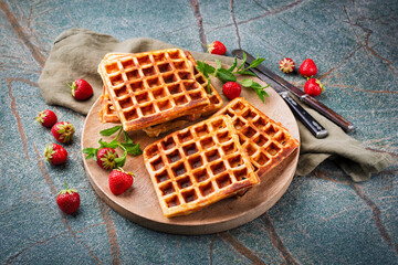 Fresh baked homemade Brussels waffles with fresh strawberries served as close-up on a wooden plate