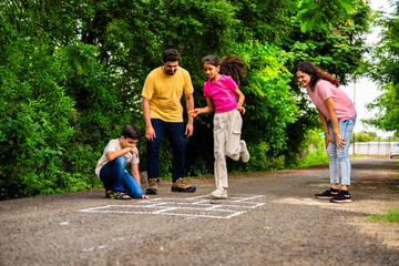 Indian family playing hopscotch or Tikkar Billa outdoors, spending joyful time in garden