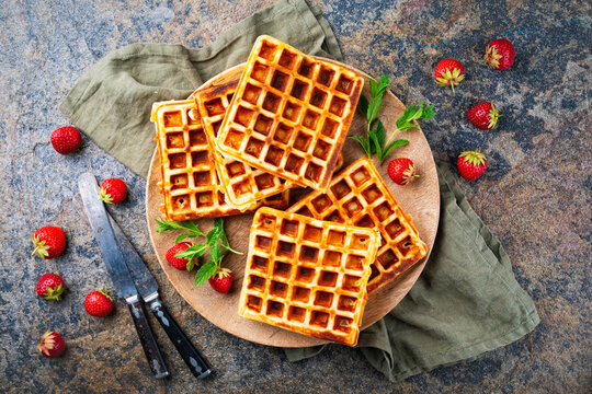 Fresh baked homemade Brussels waffles with fresh strawberries served as top view on a wooden plate