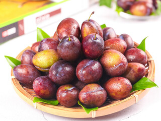 Fresh Red Plums in Bamboo Basket with Water Droplets and Green Leaves