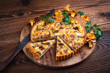 Authentic French tart with fresh chanterelles served as close-up on a wooden board © HLPhoto