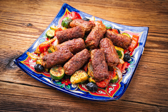 Traditional Croatian cevapi spicy meat ball rolls with troasted vegetables served as close-up on rustic plate