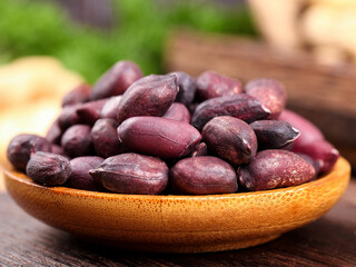 Purple-skinned peanuts in wooden bowl on rustic wooden board - healthy nuts snack ingredient