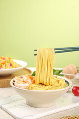 Fresh wheat noodles with shrimp in bowl lifted by chopsticks, homemade Asian ramen soup meal