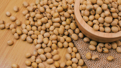 Dry soybeans in a wooden bowl and scattered on wooden table with burlap fabric, natural plant-based protein ingredient for healthy food products.