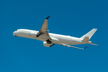 An airplane in mid air, with its landing gear retracted after takeoff, against a solid blue sky.