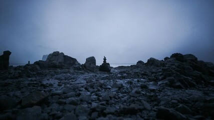 A rocky beach is illuminated by the fading light of twilight. Balanced stones rise amidst a rugged shoreline, creating a peaceful yet mysterious atmosphere in the dusk.