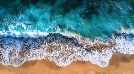 An aerial perspective captures the dynamic movement of ocean waves crashing onto a sandy beach.