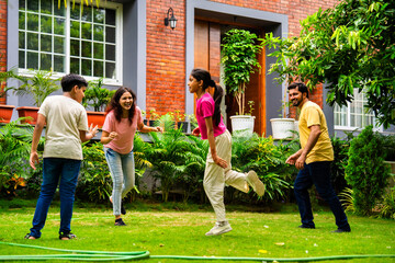 Fototapeta premium Indian family playing Langdi or one-leg hop game in garden, enjoying energetic outdoor fun