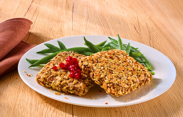 Vegetarischer Bratling mit gruenen Bohnen und Preiselbeeren auf hellem Holzfond, Tellergericht, vegan, 